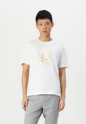 T-shirt blanc en coton, avec un design graphique beige carré au centre. Manches courtes, col rond, coupe décontractée.