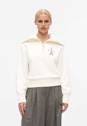 White zip-up sweatshirt with a high collar, featuring an embroidered Eiffel Tower design in purple. Soft material and relaxed fit.