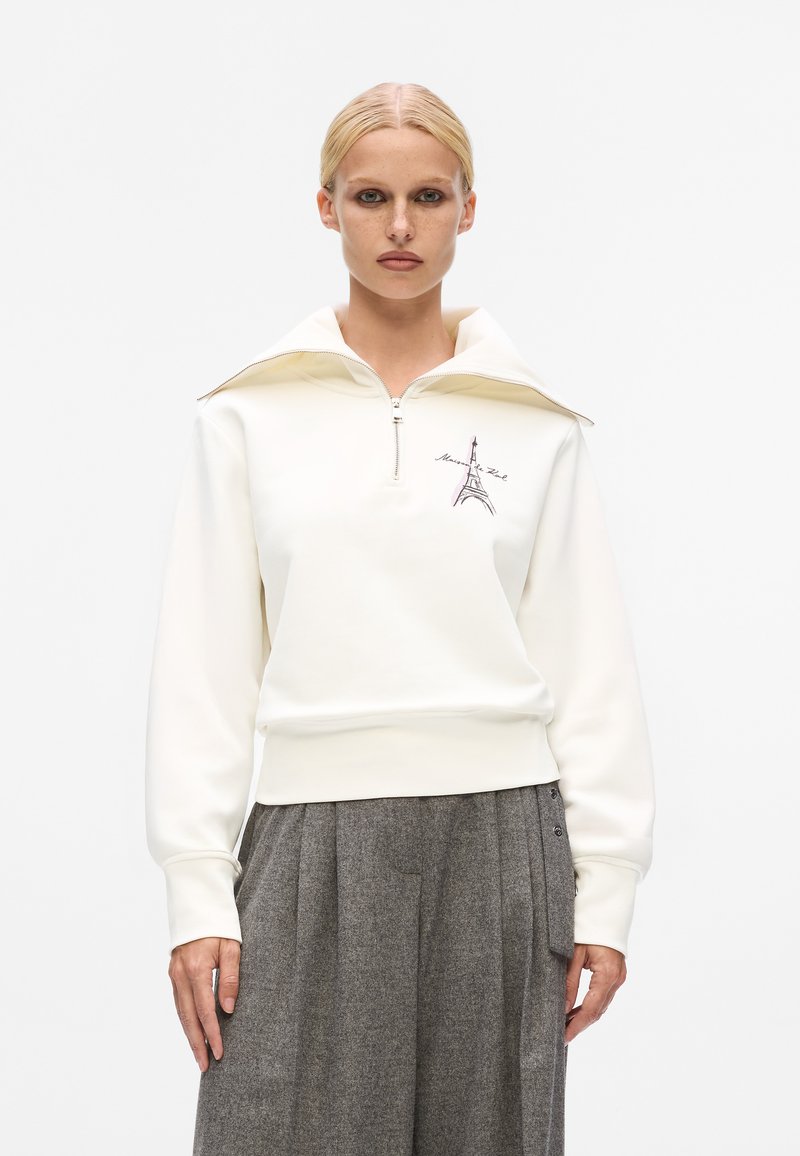 White zip-up sweatshirt with a high collar, featuring an embroidered Eiffel Tower design in purple. Soft material and relaxed fit.