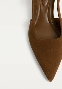 Pompa in suede marrone a punta con un elegante design a taglio e un rivestimento interno liscio. Presenta un tacco alto e affusolato per una silhouette elegante.