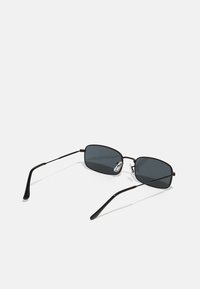 Schwarze Sonnenbrille mit rechteckigem Rahmen, dunklen Gläsern und schlanken Metallbügeln. Der Rahmen weist eine sanfte Krümmung und verstellbare Nasenpolster auf.