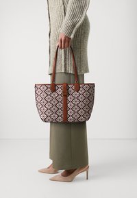 Brauner Tragetasche mit lila Blumenmuster auf hellen Hintergrund, mit glatter Textur und kontrastierenden braunen Akzenten.