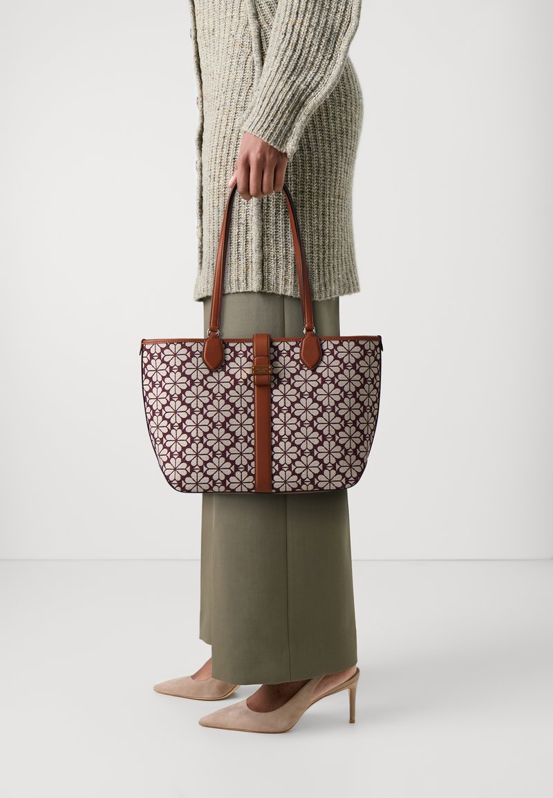Brauner Tragetasche mit lila Blumenmuster auf hellen Hintergrund, mit glatter Textur und kontrastierenden braunen Akzenten.