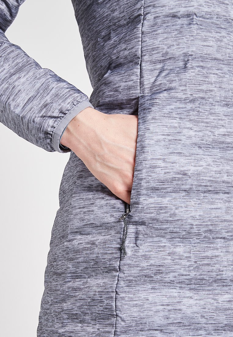 Abrigo de plumas gris con un patrón texturizado y jaspeado. Presenta un bolsillo lateral con cremallera y puños elásticos para un ajuste seguro.