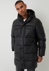 Sort dunjakke med hætte, der har et quiltet design, fire lommer foran og knaplukning. Fremstillet af skinnende, syntetisk materiale.