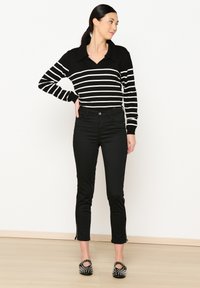 Suéter de punto a rayas blanco y negro con cuello, combinado con jeans negros ajustados con cremalleras laterales y zapatos negros con tachuelas.