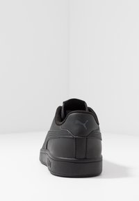 Sneakers sintetici neri con una texture liscia, design a bassa altezza e suola in gomma discreta. Presentano un logo sul tallone e dettagli di cucitura tonali.