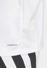 Hvid atletisk skjorte med AEROREADY-logo ved kanten, parret med sorte stribede shorts. Glat stof med en let tekstur.