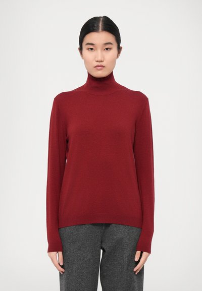 Pullover a collo alto borgogna realizzato in tessuto morbido, con maniche lunghe e vestibilità comoda. Abbinato a pantaloni grigi con fantasia.