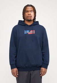 Marineblå hettegenser, myk stoff, frontlomme, snor i hetta, hvit og rød logo "JACK & JONES" på brystet, ribbestrikkede mansjetter og nederkant.