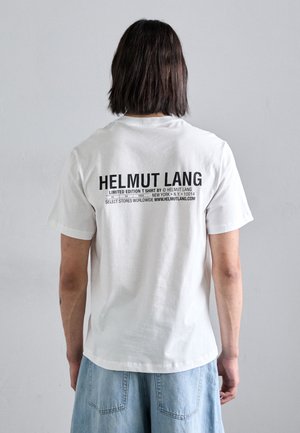 Valge puuvillane T-särk lühikeste varrukatega. Seljal on julge must tekst: "HELMUT LANG," "PIIRATUD VERSIOON," ja muud detailid erinevates suurustes.