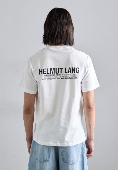 T-shirt en coton blanc avec des manches courtes. Le dos présente un texte noir en gras : "HELMUT LANG," "ÉDITION LIMITÉE," et d'autres détails de tailles variées.