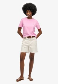 Lyserød bomulds t-shirt med brystlomme, beige denim shorts med franje kanter og brune slidesandaler med runde udskæringer.