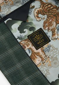 Tessuto slim-fit con un motivo a quadri verdi accostato a un design floreale e a strisce di tigre in tonalità beige e colori smorzati. Etichetta del brand nera visibile.