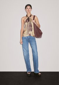 Hnědý a béžový vzorovaný halter top, modré džíny a černé platformní sandály; nese texturovanou burgundskou kabelku přes rameno. Bílý pozadí.