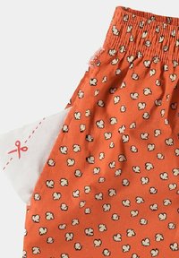 Tissu orange avec un motif de pop-corn, doté d'une taille élastiquée et d'une étiquette sur le côté. Texture douce et design léger.
