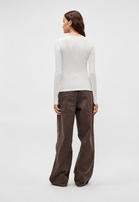 Ilgos rankovės šviesiai pilkos spalvos palaidinė ir laisvos rudos spalvos kelnės. Palaidinė turi apvalią iškirptę; kelnėse yra šoninės kišenės ir laisvas kirpimas. Lygus audinys.