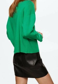 Groene oversized trui in een ribgebreide stof, gecombineerd met een zwarte leren mini-jurk met een achterzak en een gladde textuur.