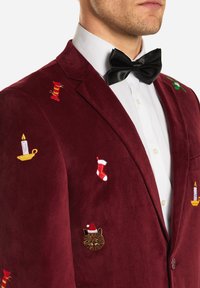 Burgundy corduroy blazer features colorful holiday-themed embroidery, including a cat, stockings, candles, and a wrapped gift. Black bow tie.