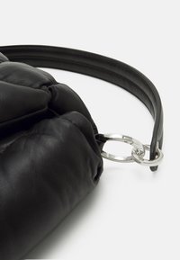 Svart läderväska med en texturerad yta, med detaljer av silvermetallring och ett runt handtag för enkel bärning.