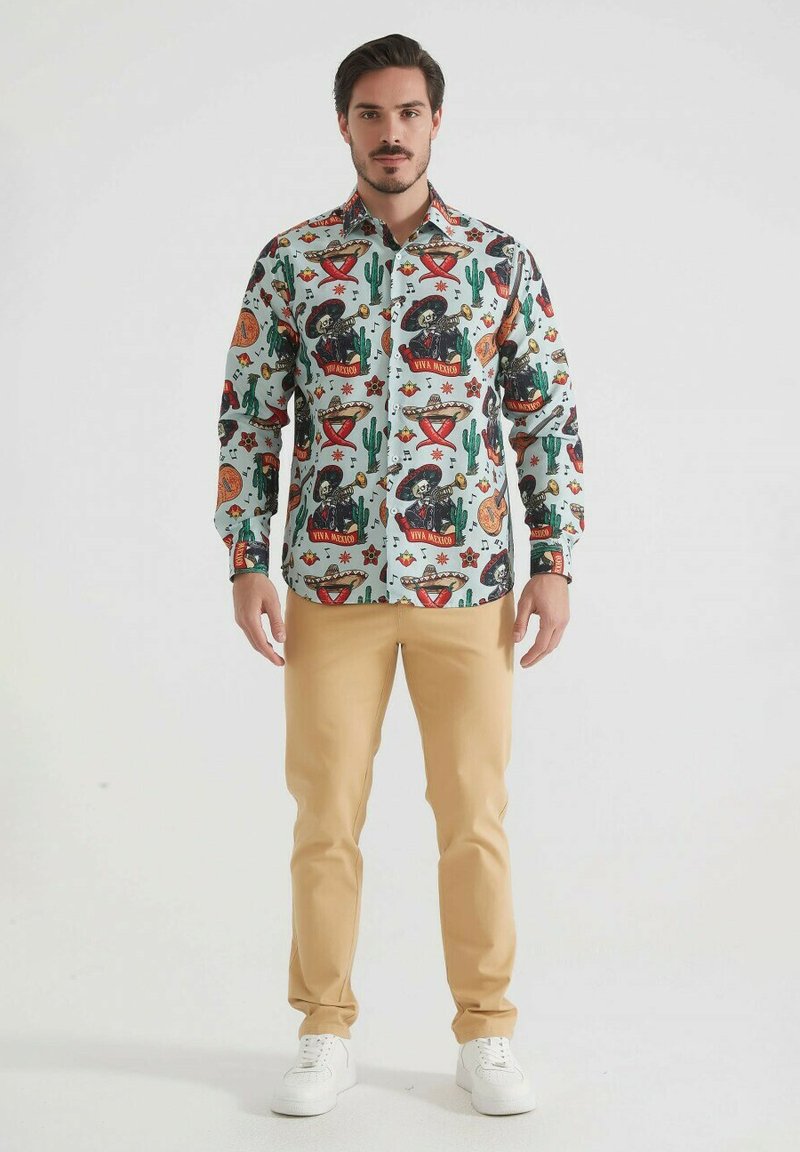Chemise colorée à manches longues avec un fond clair et divers motifs, y compris des cactus, des maracas et du texte, associée à un pantalon beige.