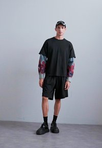 Black oversized T-shirt with colorful sleeves, black shorts, and chunky black sneakers. Accessories include a cap and ankle socks.