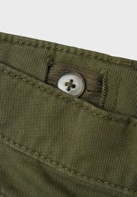 Olivgrüner Stoff mit feiner Rippung; verfügt über einen Metallknopf mit einem vierlagigen Design und einer Stichverzierung am Rand der Tasche.