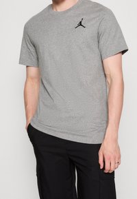 Šedé tričko s krátkým rukávem vyrobené z bavlněné směsi, na hrudi s černým logem Jumpman. Měkká textura a volný střih.