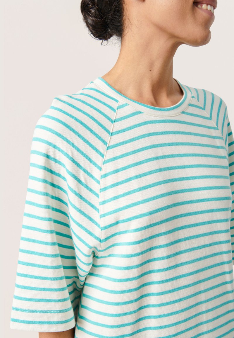 Tricou cu mânecă scurtă și guler rotund, cu dungi orizontale albastre deschise și albe. Confecționat dintr-un material moale, cu o croială lejeră și mâneci raglan.