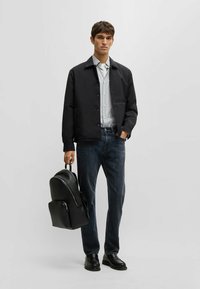 Svart jacka, randig skjorta, mörka jeans. Svart läderryggsäck med texturerad yta. Svarta skor. Enkla, funktionella designelement.