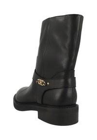 Černá kožená bota po lýtko s nízkým stohovaným podpatkem a zlatým emblémem na bočním pásku na bílém pozadí.