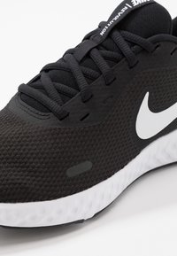 Scarpa sportiva nera con tomaia testurizzata, caratterizzata da un logo Nike bianco, lacci neri e una suola bianca con un design ammortizzato.