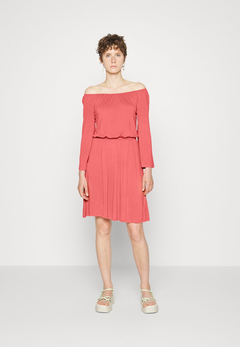 Vestido coral com ombros à mostra, mangas longas, cintura ajustada e saia fluida, feito de tecido macio. Combinado com sandálias de plataforma leves.