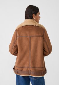 Braune Wildlederjacke mit einem tanfarbenen Kunstfellkragen, kontrastierenden Nähten, einer taillierten Taille und einem lässigen Schnitt.