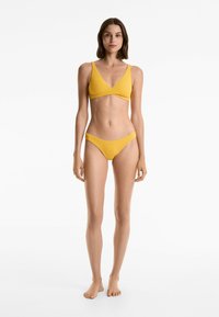 Gul ribbad bikiniuppsättning med en V-ringad bralette och låga trosor. Tyget har en texturerad yta och är elastiskt.