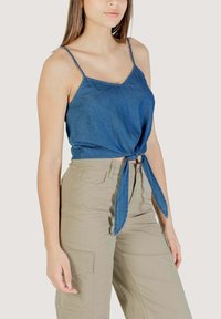 Top corto in denim con spalline regolabili, dettaglio a nodo in vita, di colore blu medio; abbinato a pantaloni cargo beige chiaro.
