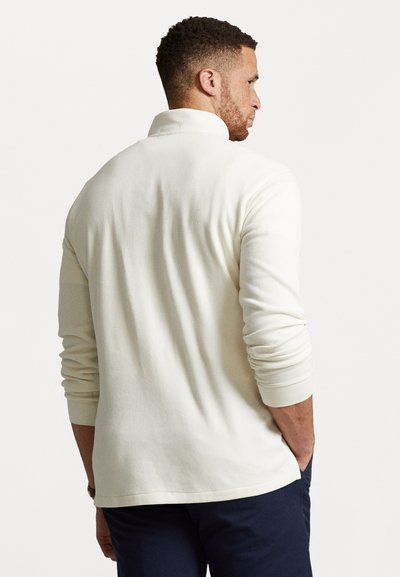Lichtromige poloshirt met lange mouwen, rechte kraag, ribgebreide manchetten en een relaxte pasvorm, weergegeven van achteraan. Soepele textuur.