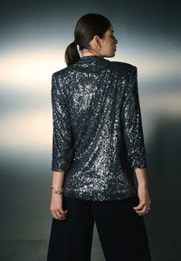 Čierne sako s flitrami s trojštvrťovými rukávmi a vystužením na ramenách, s textúrovaným povrchom a voľným strihom.