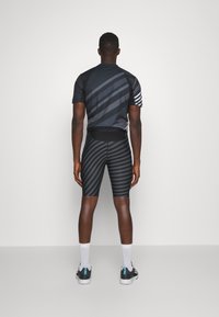 Camiseta deportiva negra y pantalones cortos a juego, con rayas diagonales. La camiseta tiene mangas cortas y los pantalones cortos son ajustados.