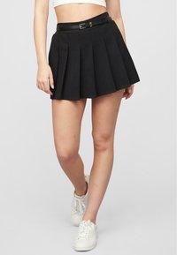 Svart plisserte skjørt med belte som har spenne, laget av en strukturert stoff. Kombinert med hvite sneakers, og viser en A-linjeform.