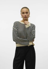 Gestreepte gebreide trui in crème, marineblauw en beige, met een losse pasvorm, verlaagde schouders en geribde manchetten, gecombineerd met zwarte broeken.