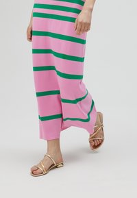 Rosa randig klänning med djärva gröna ränder, tillverkad av mjukt tyg, ihop med glänsande guldsandaler med korslagda remmar.