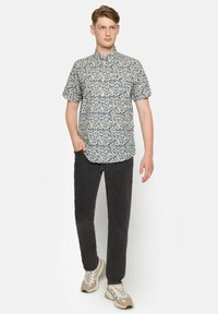 Camisa de manga corta en crema con patrón de hojas azules, con cuello abotonado, combinada con pantalones oscuros y zapatillas ligeras.