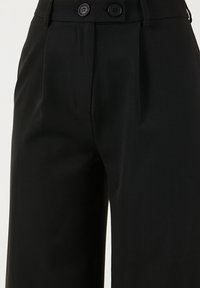 High-waisted black trousers made of smooth fabric, featuring two front buttons, pleats, and a tailored fit.