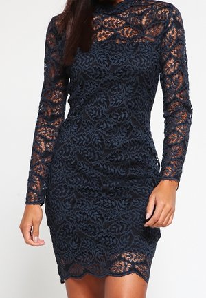 Marineblå blondekjole med lange ærmer og en tætsiddende silhuet. Har blomsterprintet tekstur og en bølget kant.