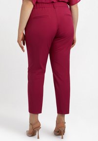 Pantaloni ajustați, până la gleznă, de culoare magenta închis, cu un brâu elastic și două buzunare la spate. Purtați cu pantofi stiletto nude.