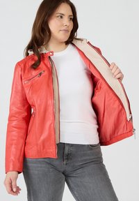 Röd läderjacka med en beige innertyg, med dragkedjefickor och en figurnära design, utställd öppen mot en neutral bakgrund.