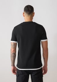 Kortærmet sort t-shirt med tekstureret stof, der har hvid kant ved ærmerne og nederste søm. Renset design uden synlige mønstre.