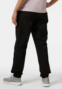 Pantalones jogger negros con puños elásticos, fabricados en material suave. Combinados con zapatillas grises claras con detalles, y una camiseta rosa.