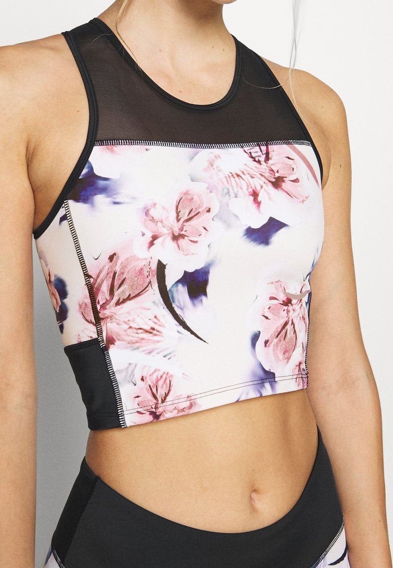 Haut court à motif floral avec un col en résille, présentant une base noire, des fleurs roses vibrantes et des coutures contrastantes le long des bords.